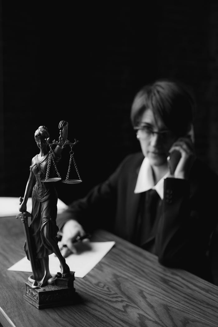 services-02 A black and white photo of a lawyer on the phone with a Lady Justice figurine in focus.